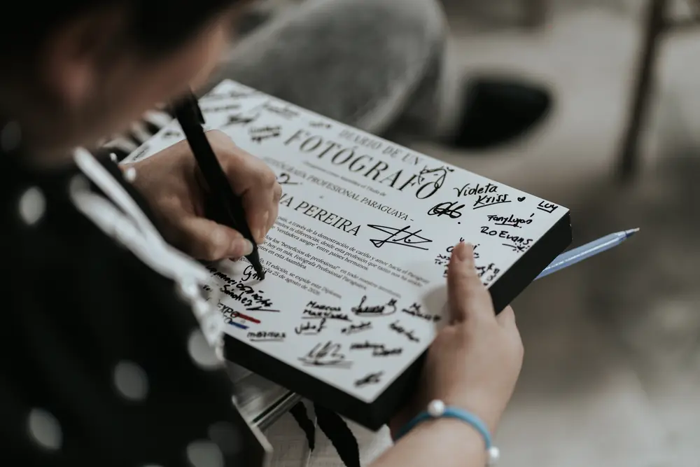 Una mano firma el póster del Diario de un Fotógrafo lleno de autógrafos
