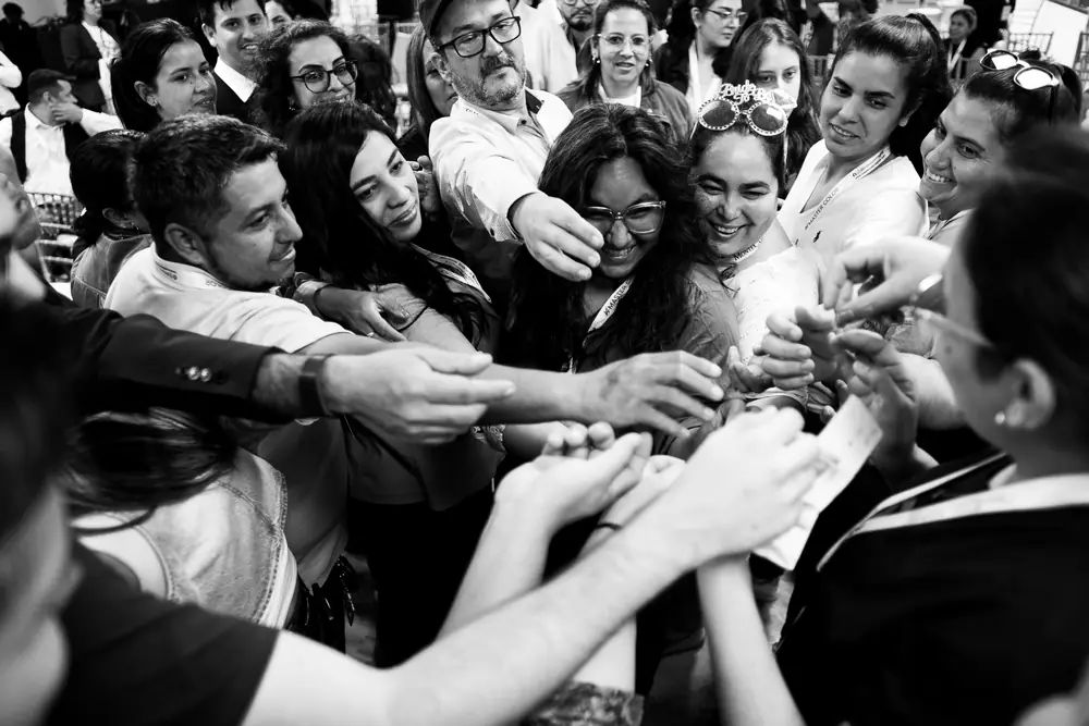 En blanco y negro, un grupo de colegas junta las manos al centro de una ronda