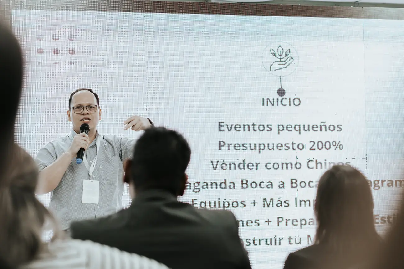 Un instructor habla con el micrófono frente a la pantalla de su charla, con el público de espaldas